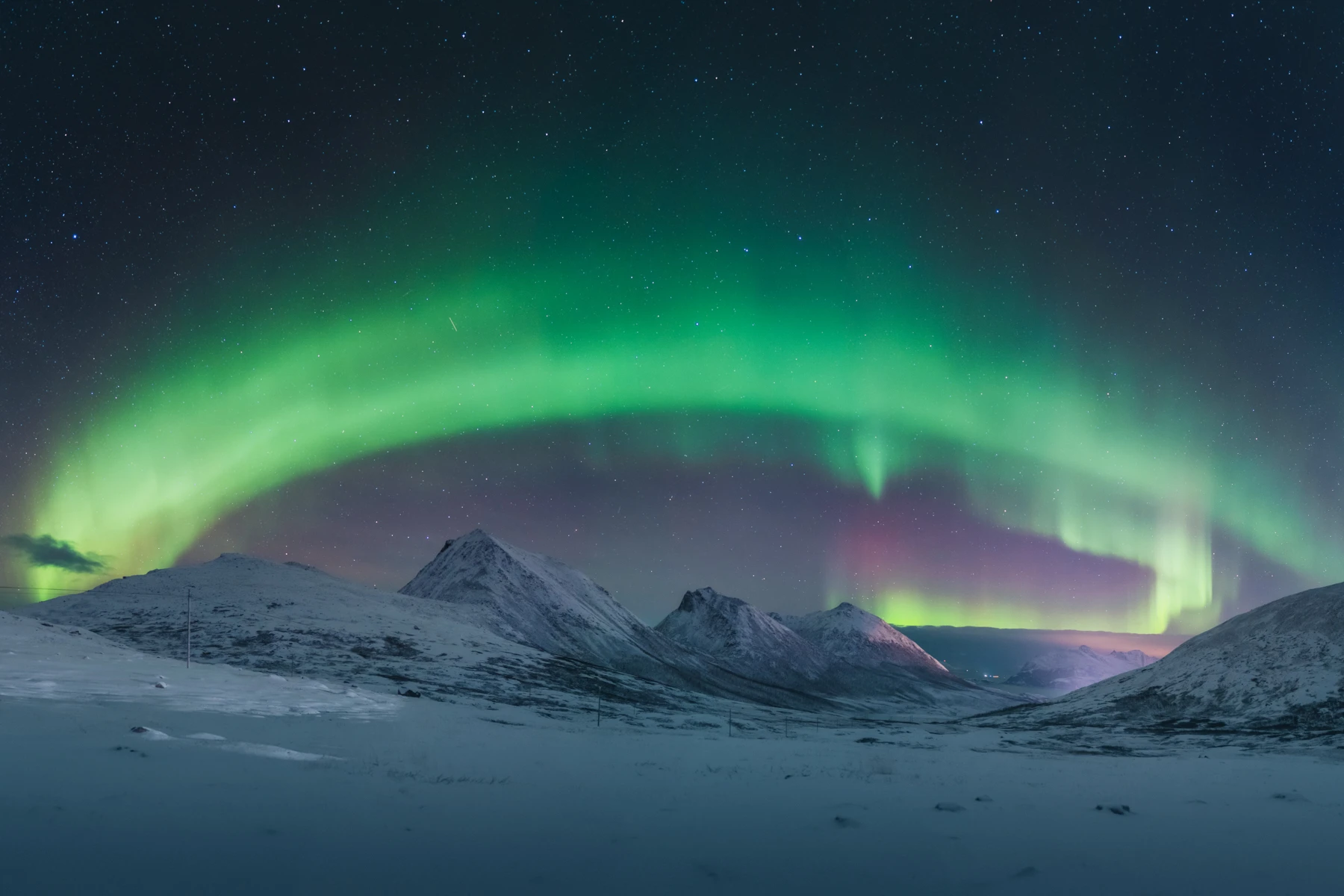 Aurora borealis shaped like a rainbow in the night sky, arching in purple and green above snow-covered mountain peaks.