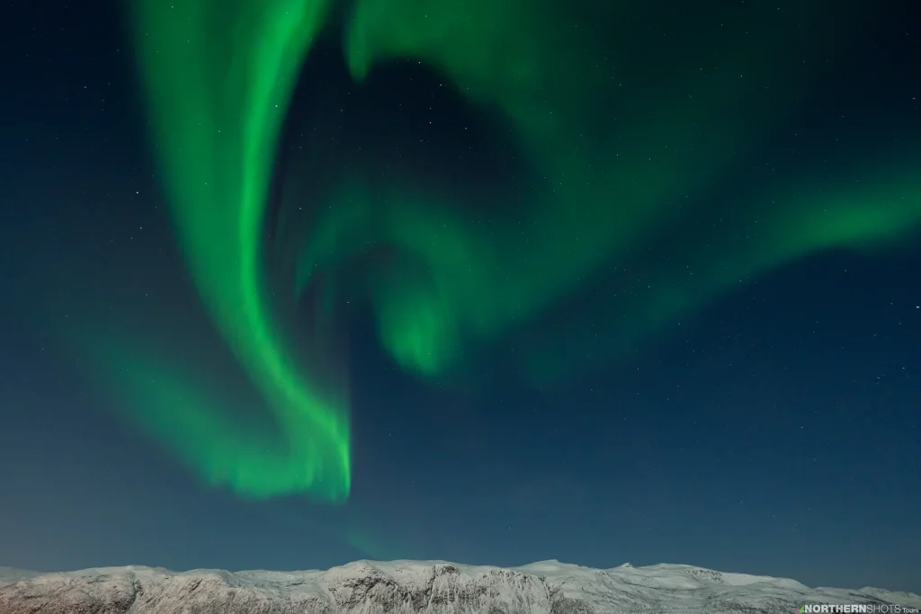 Aurora swirling above a snowy mountain range in Arctic Norway, near Tromsø