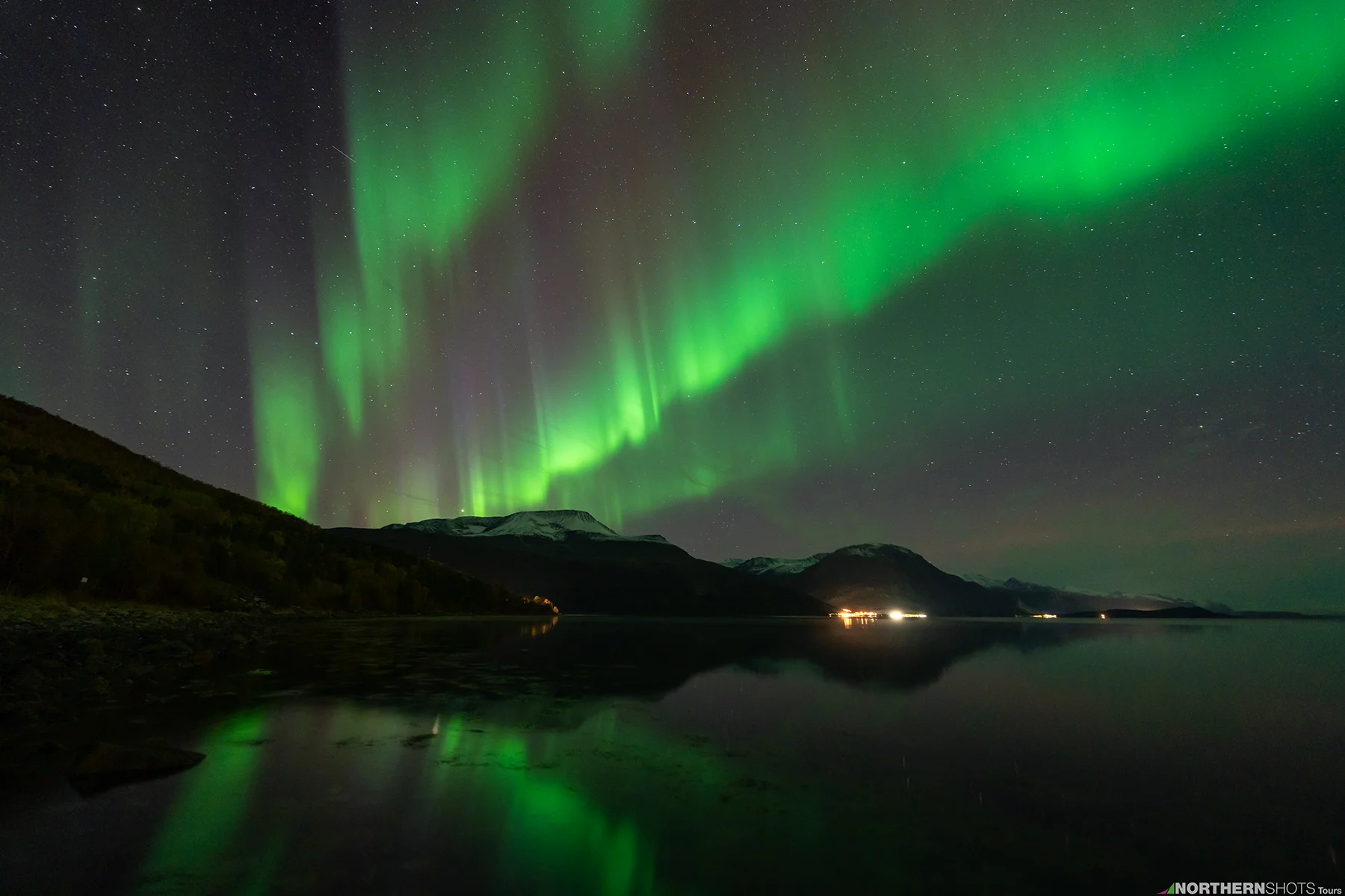 Three vivid aurora flares stretching across the night sky above a silhouetted Arctic coastline near Tromsø, Norway