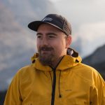 Northern Lights guide Tommy in outdoor gear standing against a softly blurred Arctic wilderness backdrop.