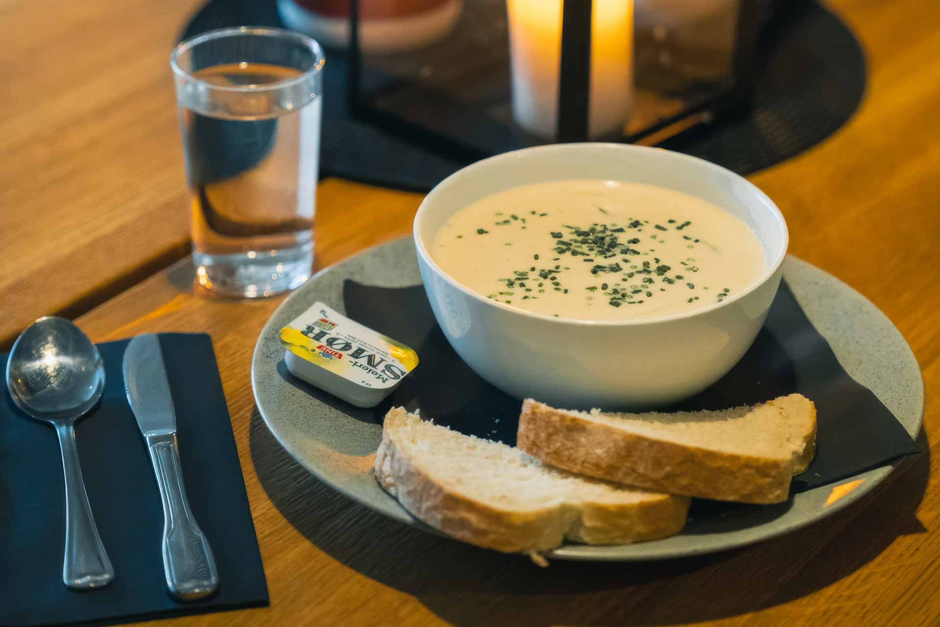 Close-up of a fish soup plate served at Sommarøy Hotel, with bread, butter, cutlery, and candlelight on a wooden table.