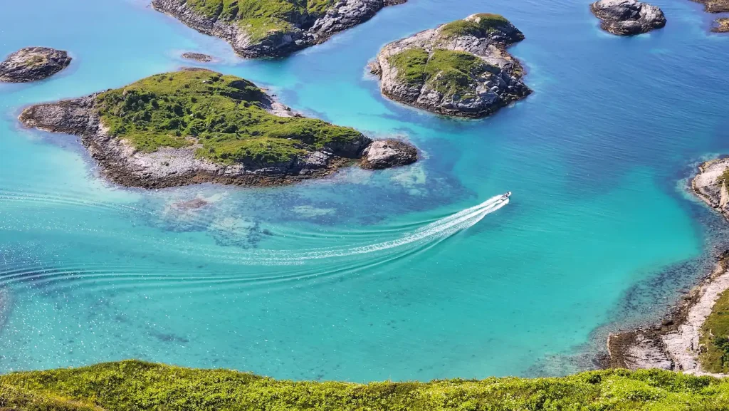 Eagle view from the top of Ørn-Fløya, overlooking a speedboat driving throught the small islands surrounding Sommarøy.
