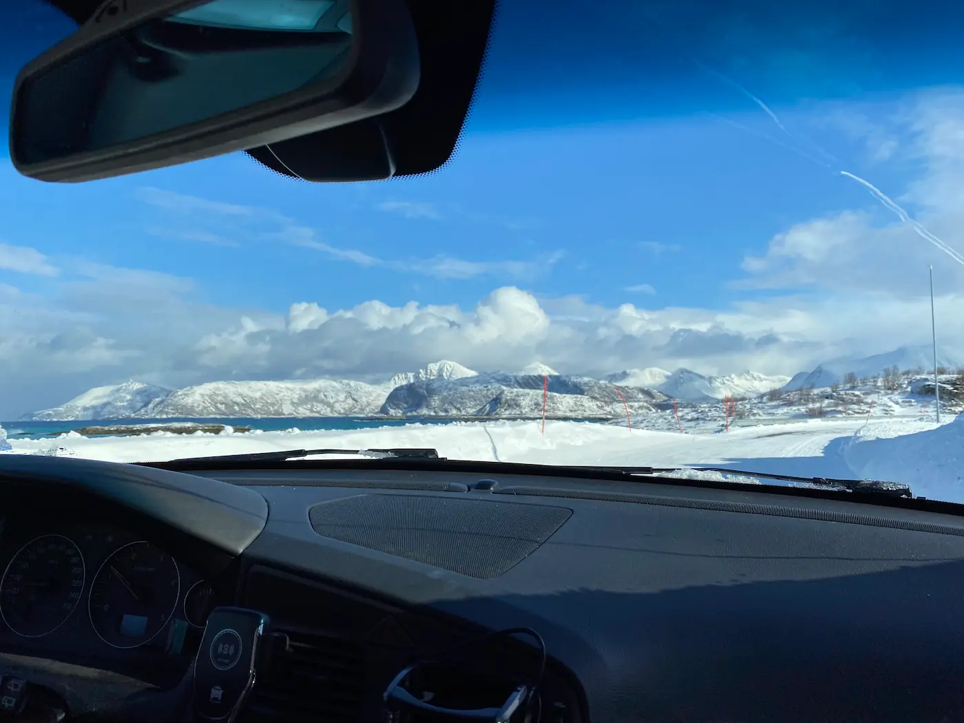 View through a car windshield during a sunny, snowy drive around Sommarøy.
